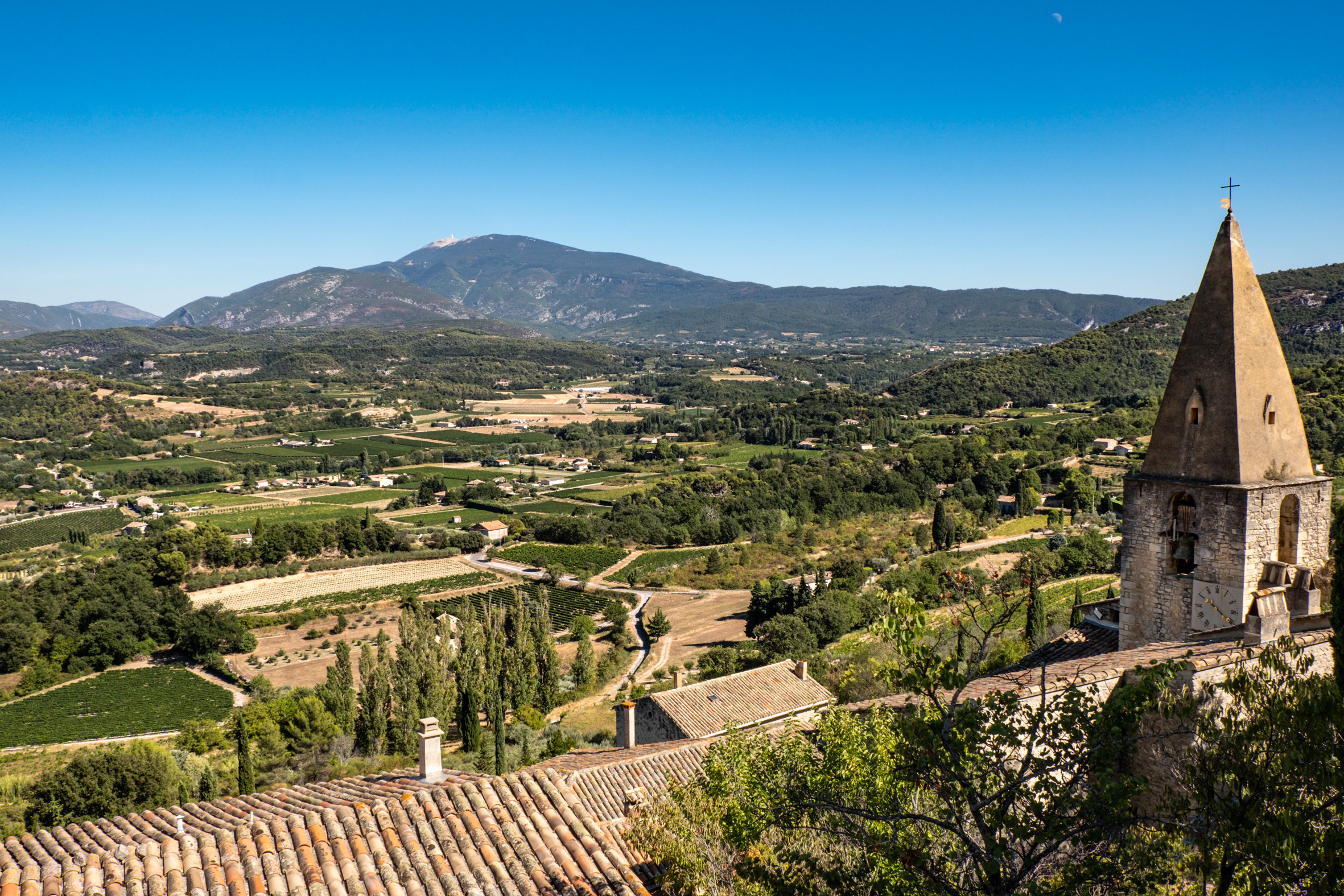 Vue sur la vallée depuis le vieux village de Crestet. Au premier plan : toits de maisons et clocher.