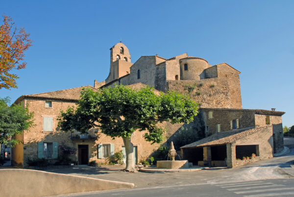 Vue sur une place avec fontaine et lavoir surplombée par l'église de Puyméras.