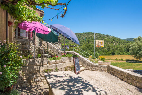 Vue de la terrasse du Bistrot de Pays de Savoillans avec ses parasols colorés et tables en pierre.