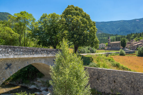 Vue sur l'entrée du village de Savoillans, avec le pont en avant plan et l'église à l'arrière plan.