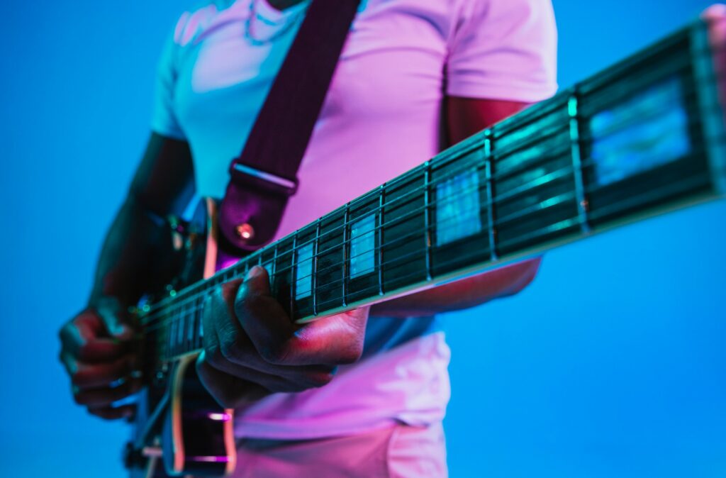 Un homme joue de la guitare électrique devant un fond bleu.