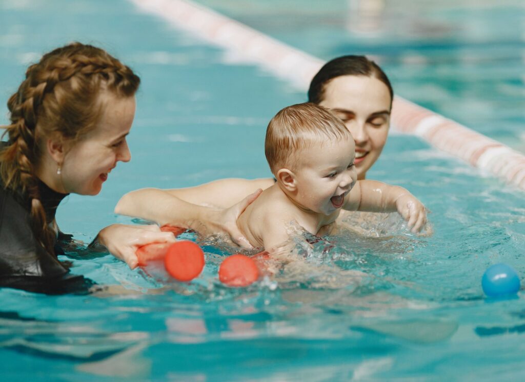 Une maman et son bébé dans une piscine en compagnie d'une maître-nageuse lors de l'activité Rencontres aquatiques proposée par la crèche Les p'tits malins à Sablet.