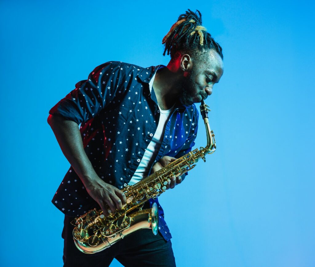 Un homme joue du saxophone devant un fond bleu.