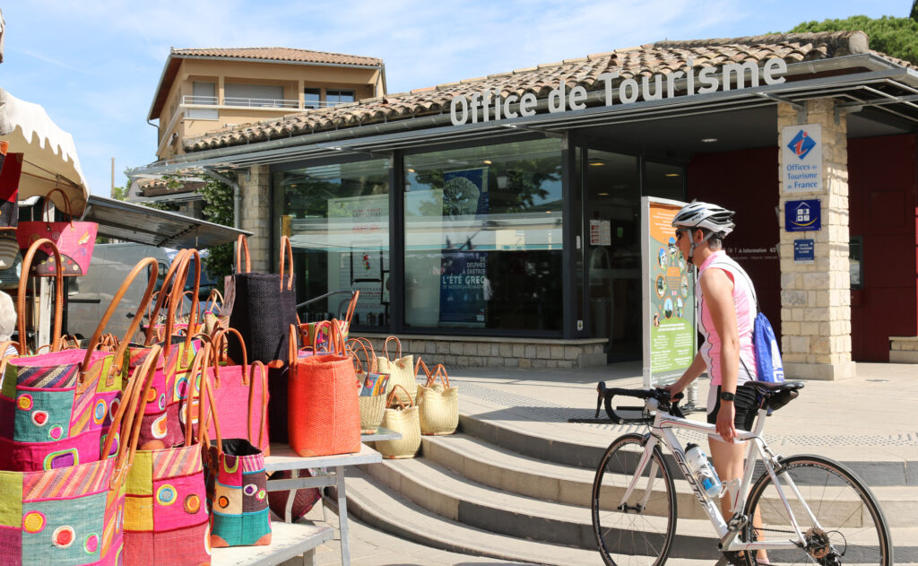 Vue de l'entrée principale de l'office de tourisme Vaison Ventoux Provence, avec un cycliste à l'arrêt au premier plan.