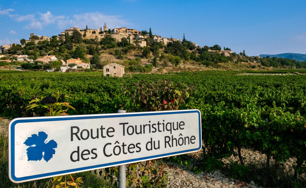 Vue sur le panneau indicateur de la route touristique des Côtes du Rhône, avec le village de Faucon en arrière plan.