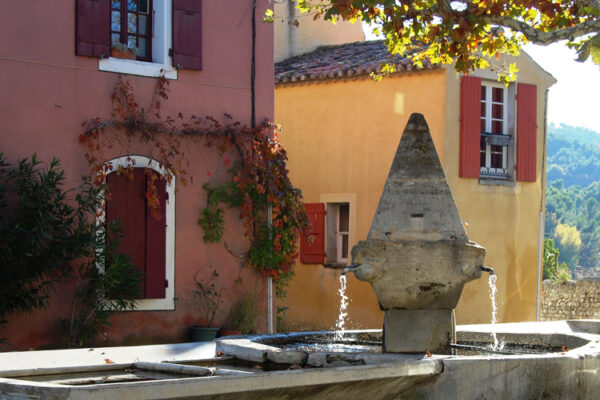 Fontaine de buisson et maisons colorées sur place principale.