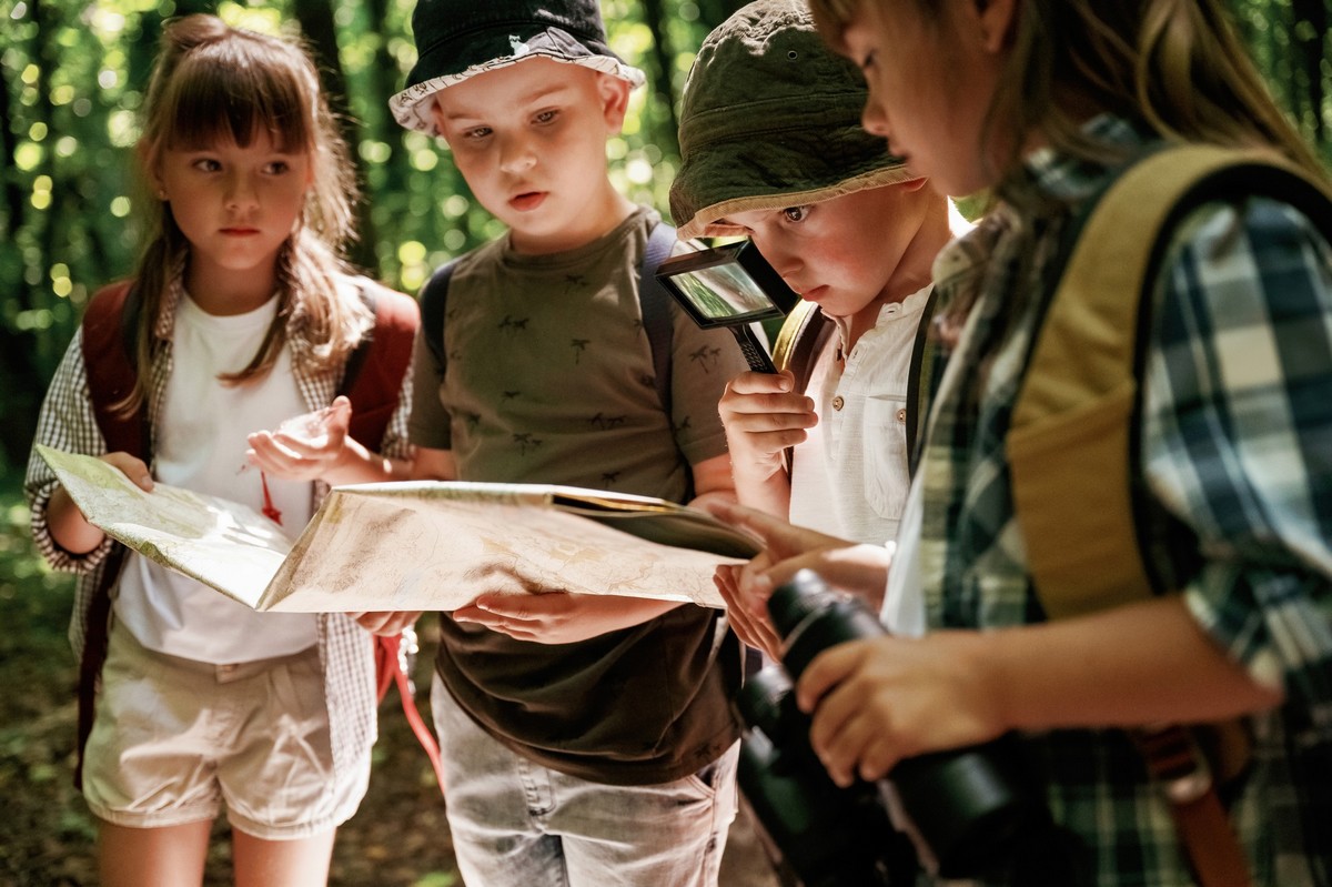 Looking at the map. Kids in forest at summer daytime together